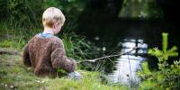 Lille dreng sidder ved en å og fisker med en hjemmelavet fiskestang