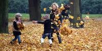 På billedet ses en mor og sine to børn, der leger 'bladregn' med visne blade i en park